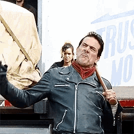 a man in a leather jacket is holding a bat in front of a truck that says truck no