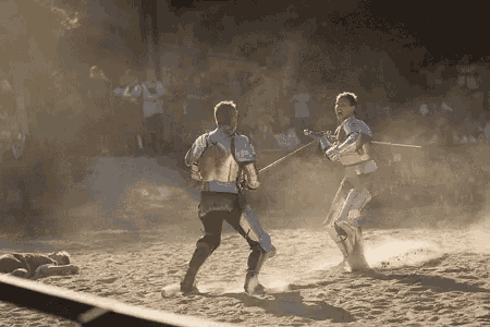 two men are fighting with swords in the sand