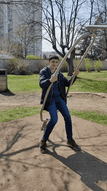 a young man in a blue jacket is sitting on a swing in a park