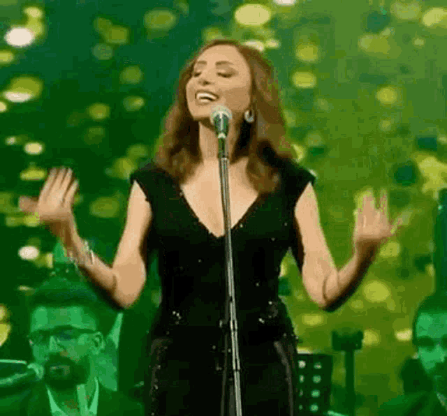 a woman is singing into a microphone on a stage in front of a green background .