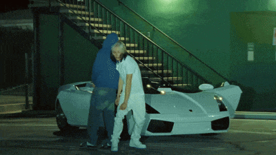 a man in a blue hoodie stands next to a woman in a white shirt in front of a white sports car