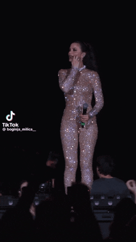 a woman in a sparkly jumpsuit is singing into a microphone in front of a crowd .