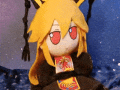 a stuffed animal with yellow hair and red eyes is sitting on a blanket .