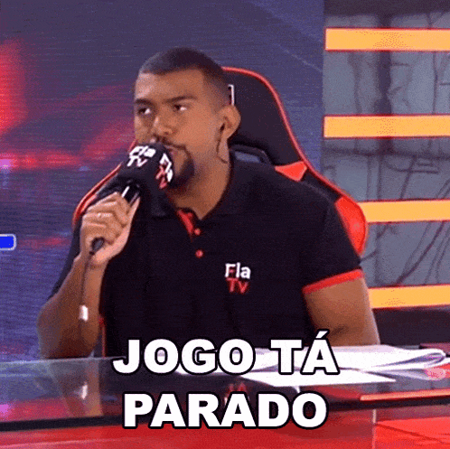 a man sitting at a desk with a microphone and the words jogo ta parado written on the bottom
