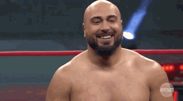 a bald man with a beard is standing in a wrestling ring smiling .