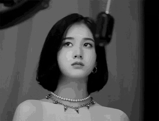 a black and white photo of a woman wearing a pearl necklace and hoop earrings .