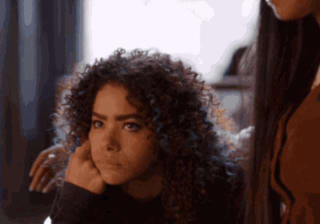 a woman with curly hair has her hand on her face while another woman looks on