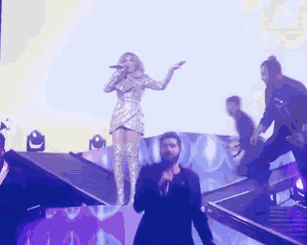 a woman singing into a microphone on a stage while a man stands behind her