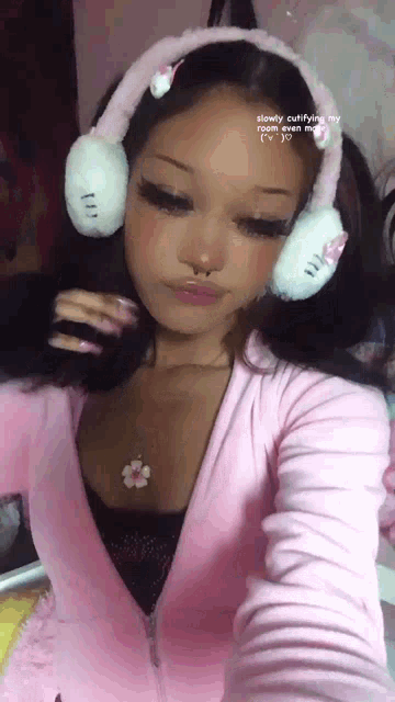 a girl wearing headphones and a pink jacket is taking a picture of herself .