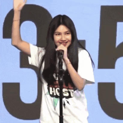 a young girl is standing in front of a microphone and waving her hand .
