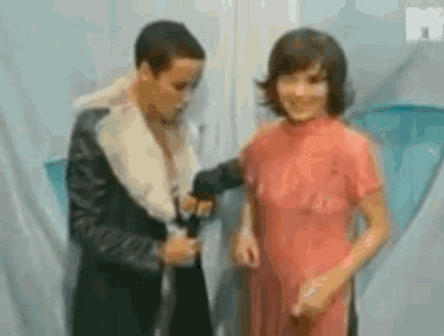 a man and a woman are standing next to each other in a room . the woman is wearing a pink dress .