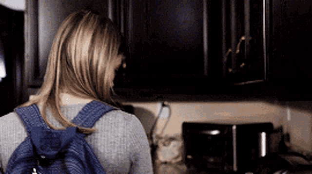 a woman with a backpack is standing in a dark kitchen