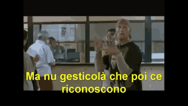 a man stands in front of a window with the words ma nu gesticola che poi ce riconoscono in yellow letters