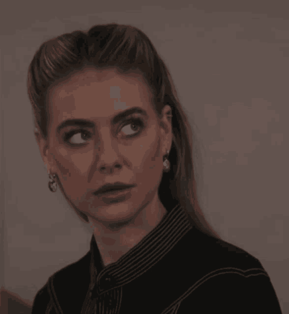 a woman wearing a striped shirt and earrings looks at the camera with a surprised look on her face