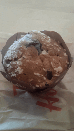 a muffin with powdered sugar on top is sitting on a paper bag that says hartons