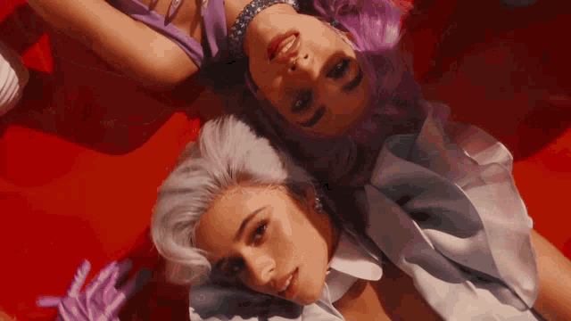 two women with purple hair are laying on top of each other on a red surface