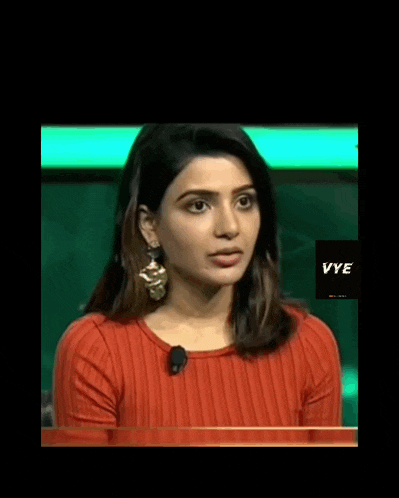 a woman wearing a red top and gold earrings is sitting at a table