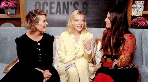 three women are sitting on a couch talking to each other and smiling .