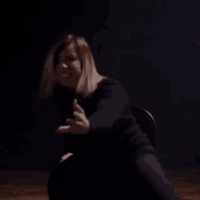a woman in a black dress is sitting in a chair in the dark .