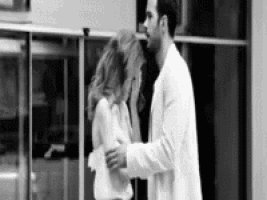 a man and a woman are hugging each other in front of a building in a black and white photo .