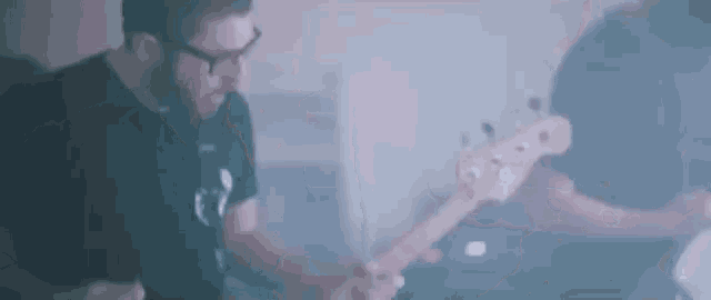 a man wearing glasses is playing a bass guitar in a room .