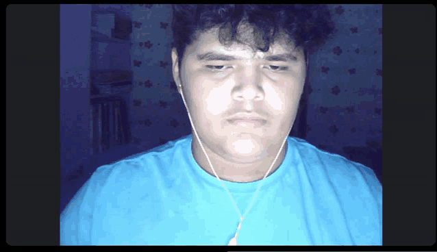 a young man wearing a blue shirt and earbuds looks at the camera