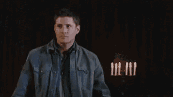 a man in a denim jacket is standing in a dark room with candles .