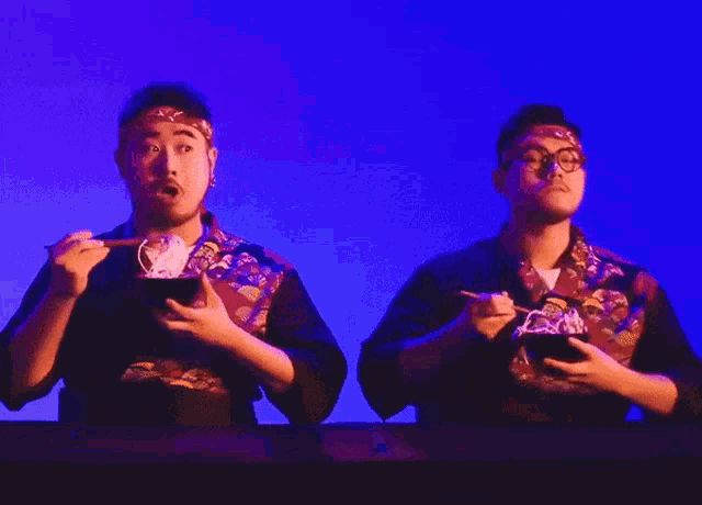 two men are eating noodles with chopsticks in front of a purple background