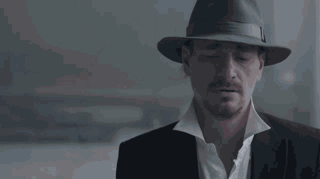a man in a fedora is being pointed at by another man holding a gun