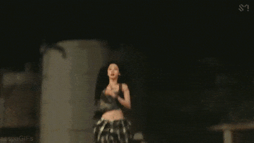 a woman in a crop top is standing in a dark room with a microphone in her hand .