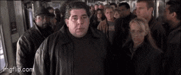 a man in a leather jacket is standing in front of a crowd of people on a bus .