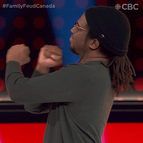 a man with dreadlocks and a beanie is dancing in front of a screen that says familyfeud canada