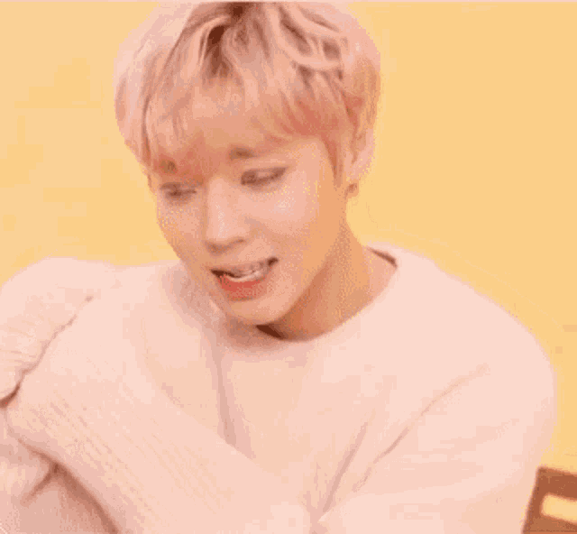 a young man with pink hair is wearing a pink sweater and making a funny face .