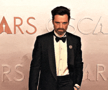 a man in a tuxedo is standing in front of a sign that says oscars