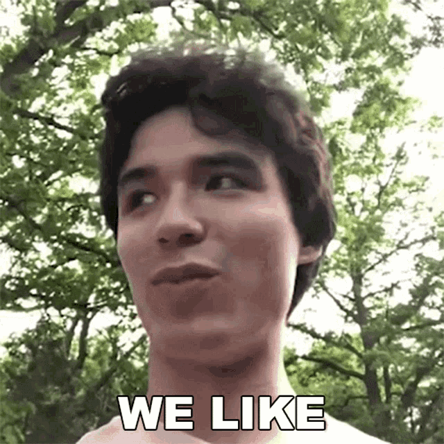 a young man is standing in front of trees and says we like