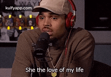 chris brown is wearing headphones and a hat while talking into a microphone .