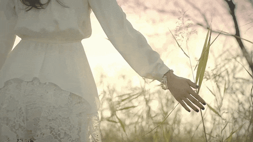 a woman in a white lace dress is standing in a field