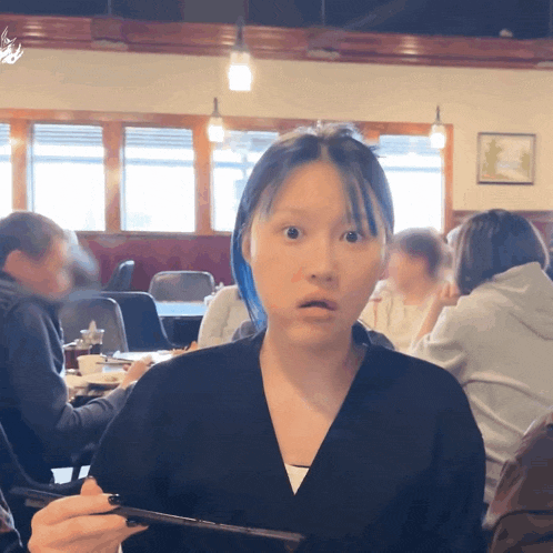 a woman with blue hair is holding a tablet in her hand and making a surprised face
