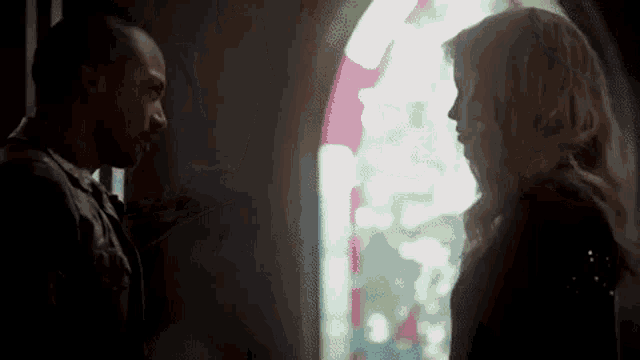 a man and woman are looking at each other in front of a stained glass window .