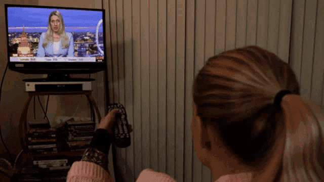 a woman is watching a news report on a tv