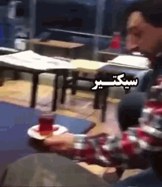 a man is sitting at a table with a cup of tea in front of him with arabic writing on it