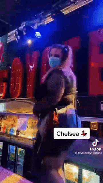 a woman wearing a mask is standing in front of a chelsea sign