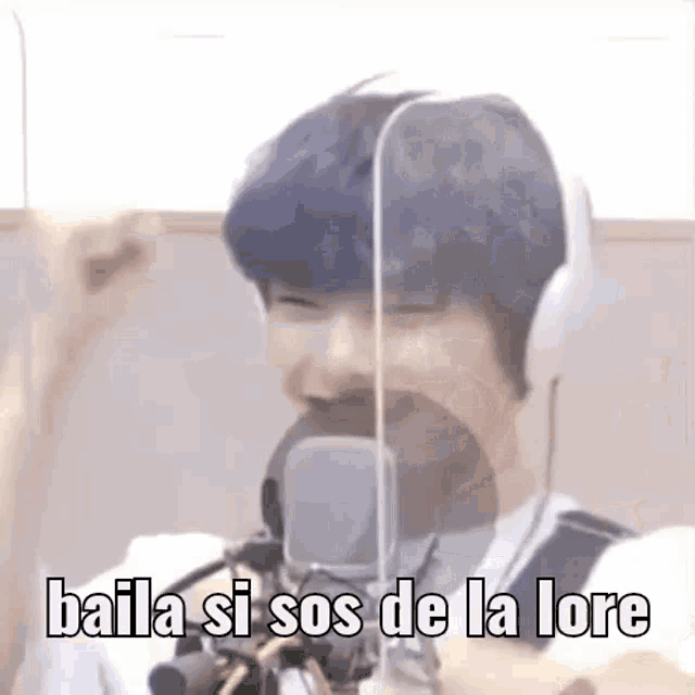 a man wearing headphones is standing in front of a microphone and saying `` baila si sos de la lore '' .