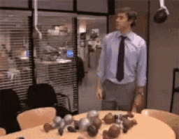 a man in a blue shirt and black tie is standing in front of a table with cupcakes on it .