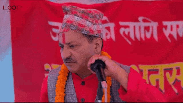 a man is speaking into a microphone in front of a red banner .