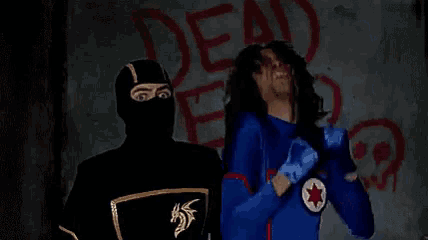 a man in a black mask is standing in front of a wall that says dead end .