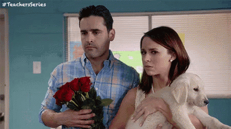 a man is holding a bouquet of roses while a woman holds a puppy .
