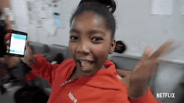 a girl in a red jacket is holding a cell phone with netflix written on it