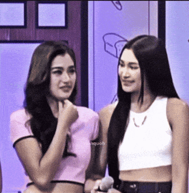 two women are standing next to each other and one is wearing a pink crop top and the other is wearing a white tank top