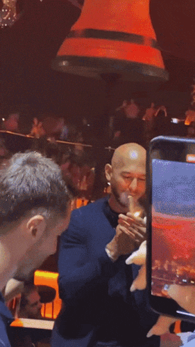 a bald man smoking a cigarette in a crowded room